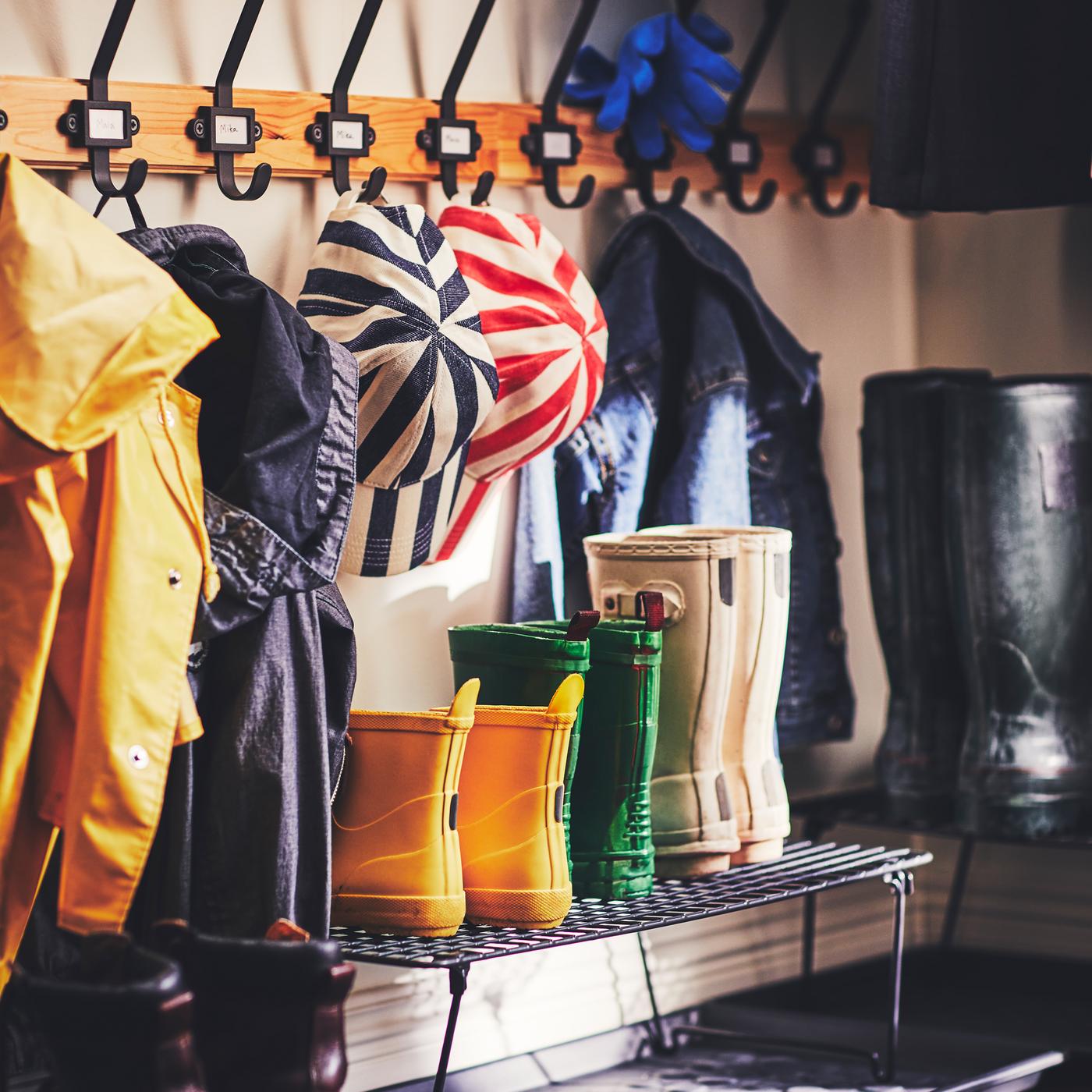 A few pairs of boots are set on a GREJIG shoe rack, which is placed on a shoe mat, below wall-mounted KARTOTEK hook racks.