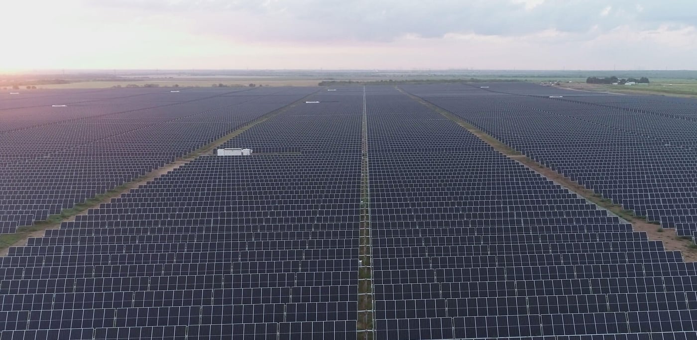 A field of endless solar panels outside with a cloudy sky above.