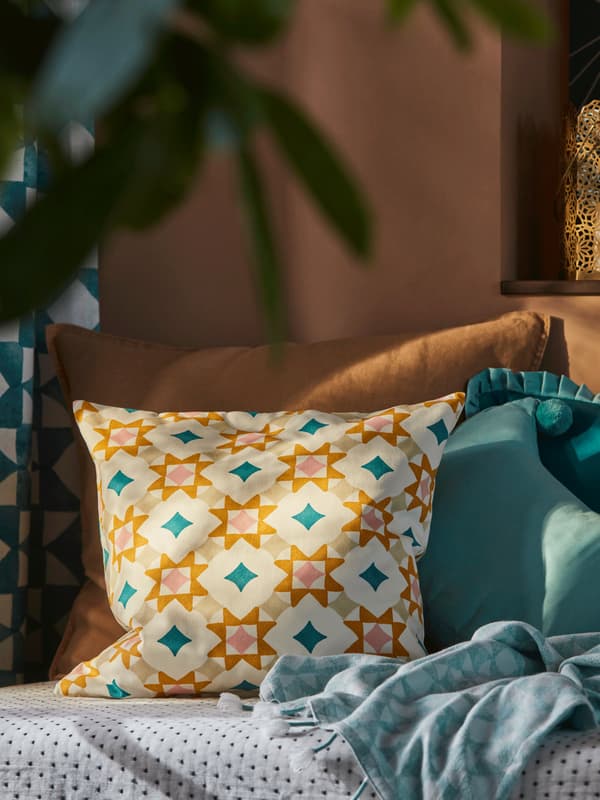 A film showing the multicolour pattern of a GOKVÄLLÅ cushion cover on a cushion placed in a brown seating furniture.