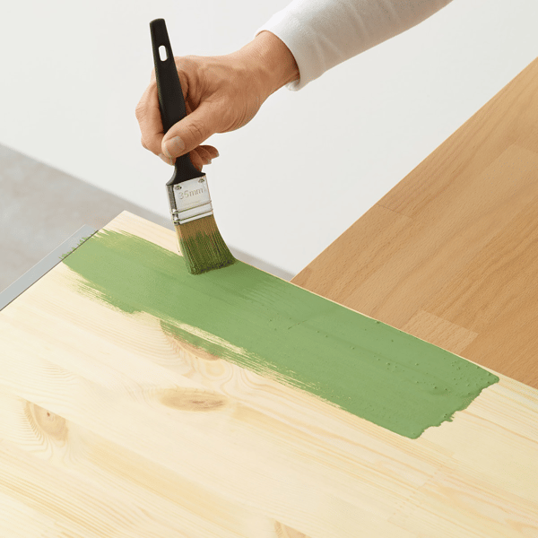 A FIXA paintbrush used to hand paint a wooden surface in green.