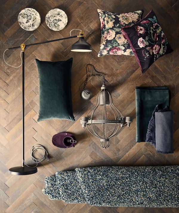 A flatlay featuring a black RANARP lamp, dark solid and SARALENA floral cushions, a rolled up green carpet, an antique ceiling lamp, and assorted bric-a-brac
