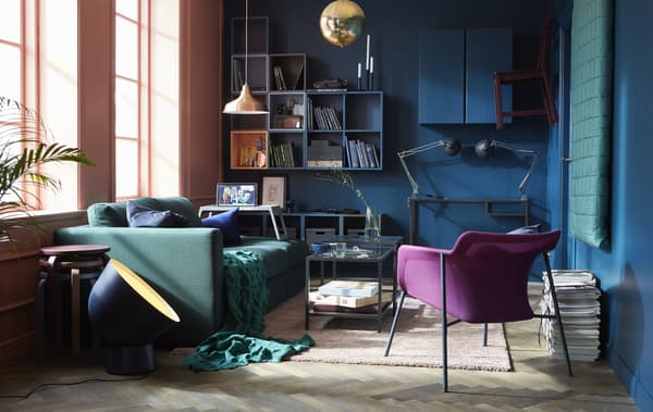 A flexible and comfortable living room that uses a modern shade of blue on the wall with a green sofa and textiles and wooden floor.