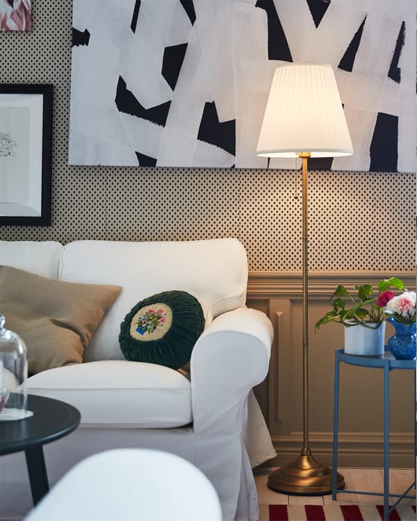 A floor lamp in brass and white is lit and is standing next to a white EKTORP sofa in a living room.