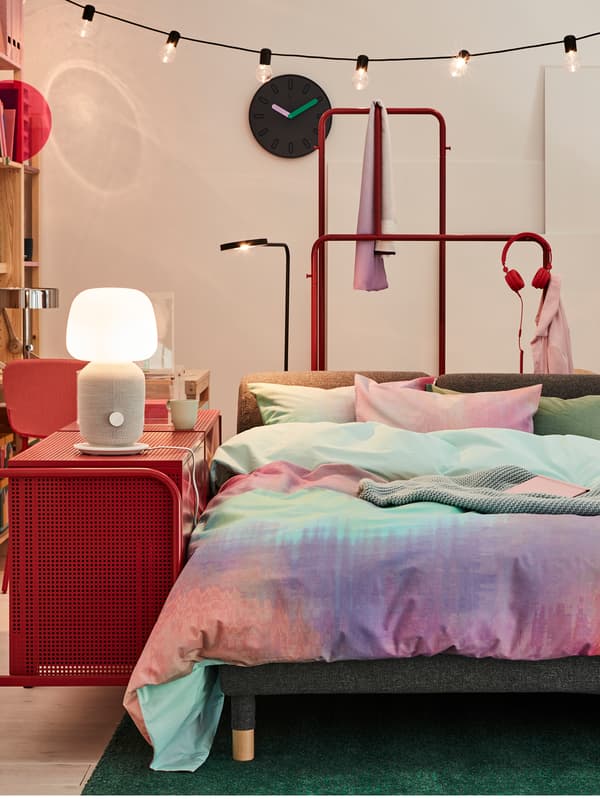 A FLOTTEBO sofa bed, turned into a bed, with colourful bed textiles and a NIKKEBY chest of drawers as a nightstand.