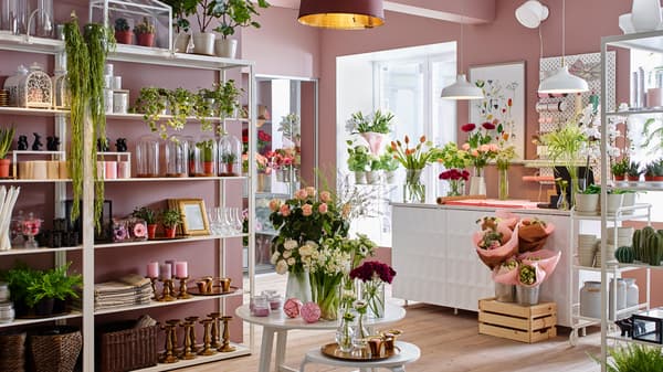 A flower shop with pink walls and furnished with FJÄLKINGE white wall shelving units to display plants and vases.