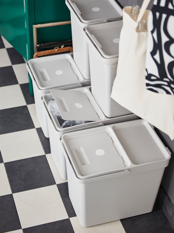 A földön öt világosszürke HÅLLBAR fedeles tároló, több egymásra van rakva, a hulladékszelektáláshoz és az újrahasznosításhoz.