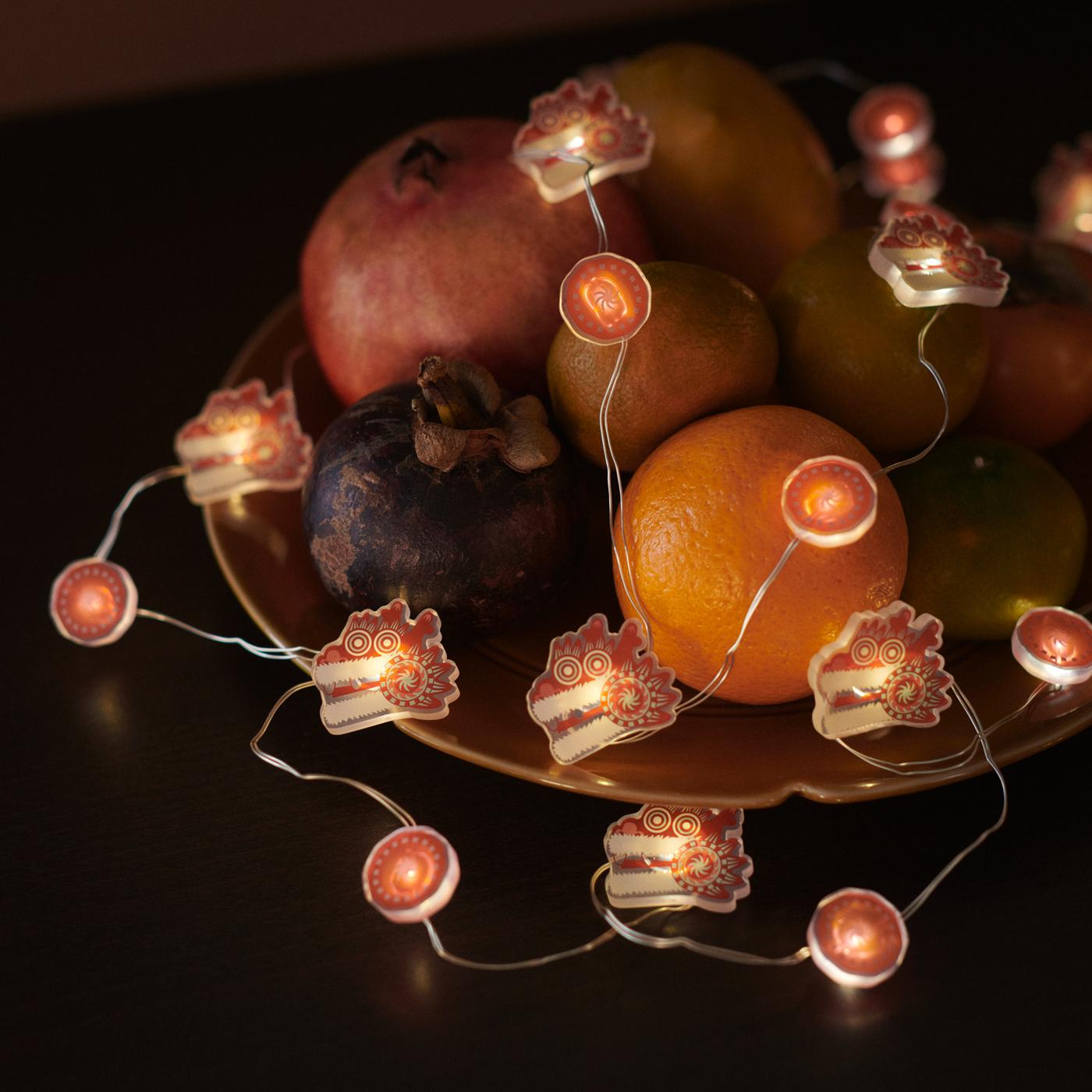 A FÖSSTA LED lighting chain draped over a selection of fruit in a yellow FÖSSTA plate.