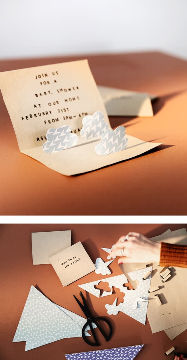 A foldable invitation to a baby shower is open to show pop-up clouds.