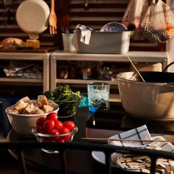 A fondue kit on a small, round table set for two on a balcony, with part of an outdoor kitchen seen in the background.