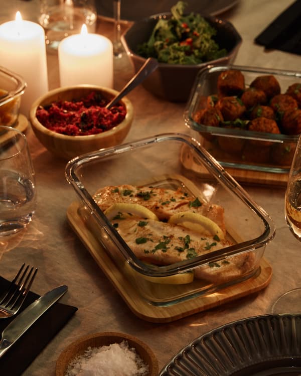 A food container made of glass placed on a table with lit candles in the background.