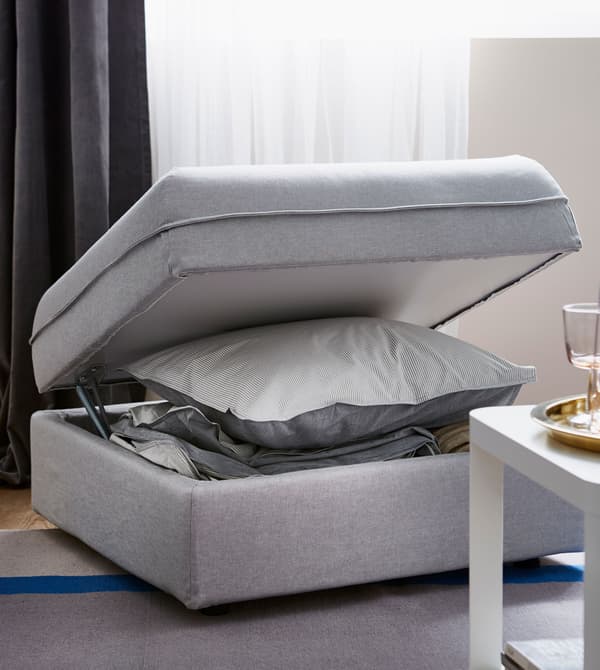 A foot stool is open to reveal bed linens inside.