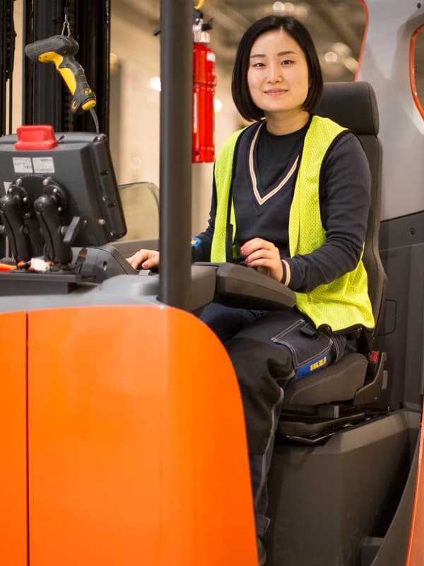 A forklift driver sitting behind the wheel while wearing a high-viz vest over her dark blue IKEA co-worker uniform.