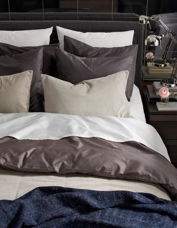 A freshly made bed with lots of pillows and layers of textiles.