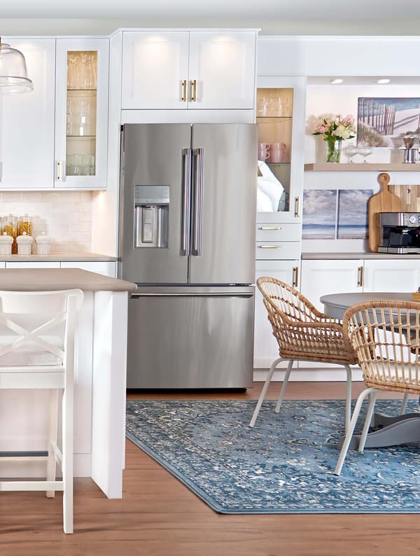 A fridge/freezer with matte white AXSTAD fronts are placed just outside a small kitchen with a black RÅSKOG trolley.