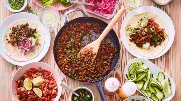 A frying pan with taco mince made from VÄRLDSKLOK plant mince next to plates and bowls with Pico de Gallo and tortillas.