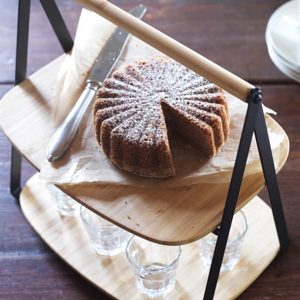 A FULLSPÄCKAD bamboo serving tray with handle, with a cake on the upper layer, and glasses below.