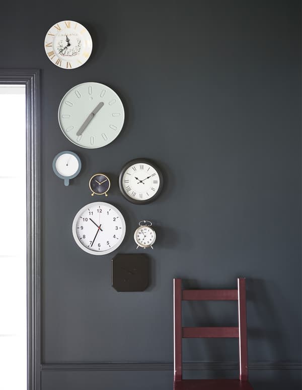 A gallery of clocks mounted on a dark grey wall.