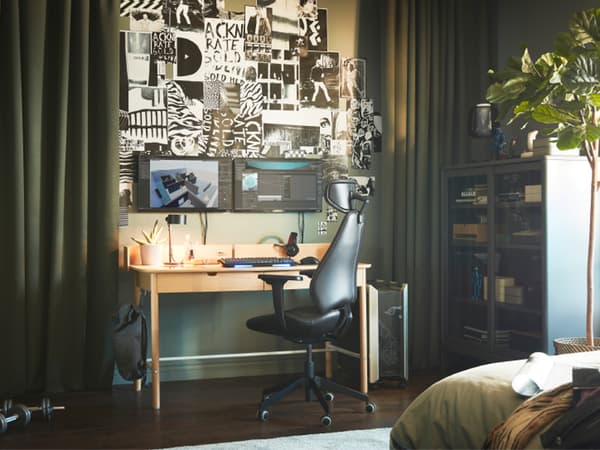 A gaming station between two green curtains. There is a picture wall with illustrations above a RIDSPÖ desk with screens.