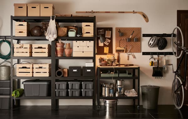 A garage wall with a black BROR shelving unit, filled with wooden, cardboard and plastic boxes in different sizes.