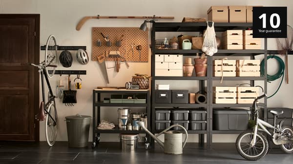 A garage wall with a black BROR shelving unit, filled with wooden, cardboard and plastic boxes in different sizes.