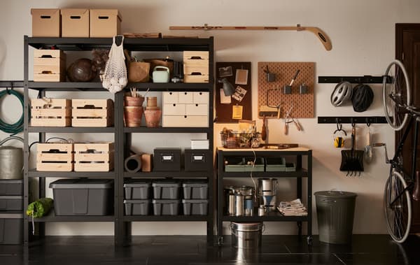 A garage wall with a black BROR shelving unit, filled with wooden, cardboard and plastic boxes in different sizes.