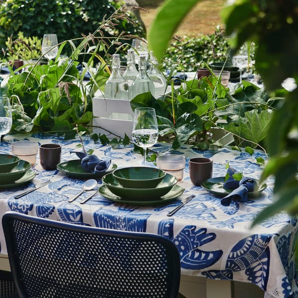 A garden dining area set with a green PELARKAKTUS deep plate on a table layered with foliage and tableware.
