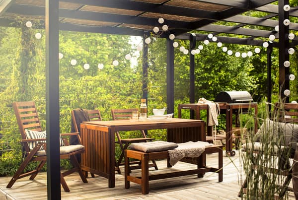 A garden with a canopy, wooden garden furniture and a barbecue from IKEA.