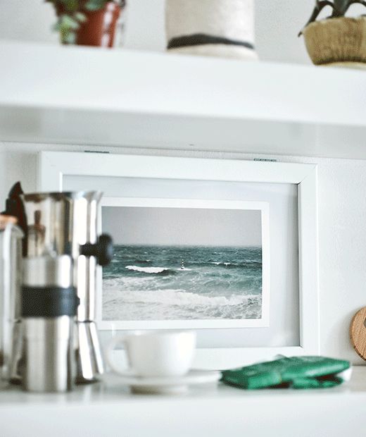 A GIF of a photograph being placed inside a frame with front-opening hinges, followed by the frame being placed on a shelf.