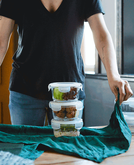A GIF of someone using a green tea towel to tie up a takeaway lunch packed in three glass containers.