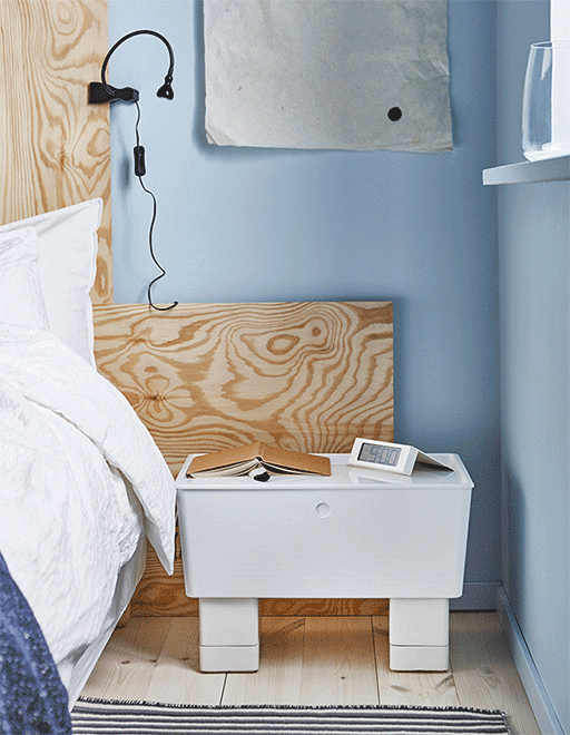 A GIF showing a nightstand made from a storage box with a lid being set onto plant pots filled with nighttime necessities 