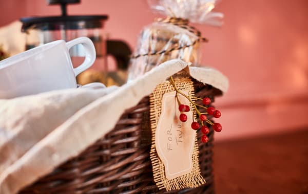 A gift-style basket with a cellophane-wrapped stack of biscuits, cups, a cafetière and decorations.