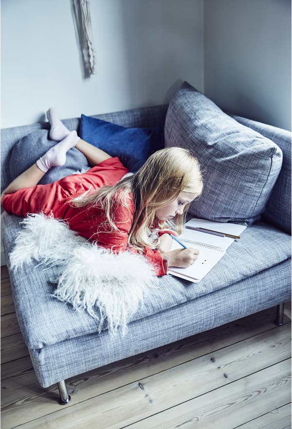A girl doing homework on a chair.