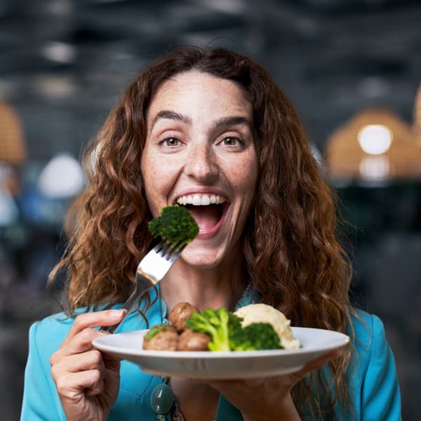 A girl holding a plate of Swedish meatballs, smiling at the camera with an open mouth, ready to eat a meatball. 