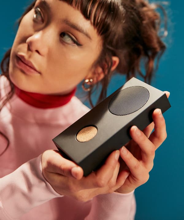 A girl holding an ENEBY wireless speaker in a careful fashion while looking away from the camera.
