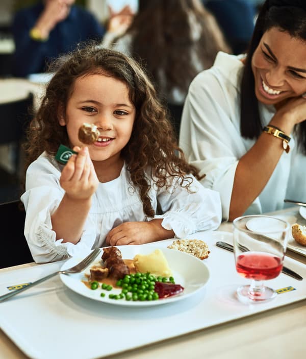 A girl is holding up a plant ball and is smiling at it. In front of her is a plate filled with plant balls, mash and peas.