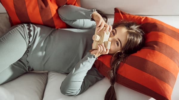 A girl relaxes happily on a sofa with the striped HILDAMARIA cushion cover in orange and brown.