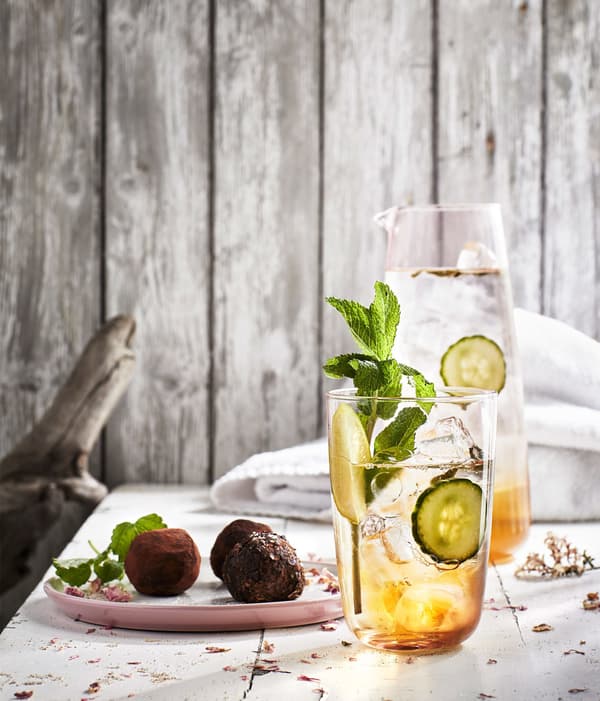 A glass and glass pitcher with yellow IKEA EGENTID tea and citrus to make lemongrass tea on the rocks.