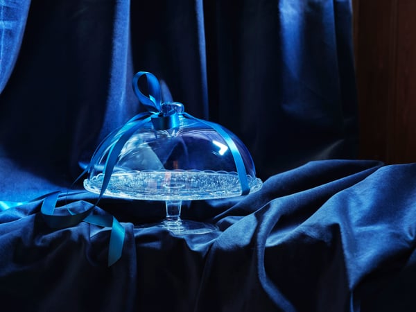 A glass cakestand, wrapped in a bow on a blue velvet background