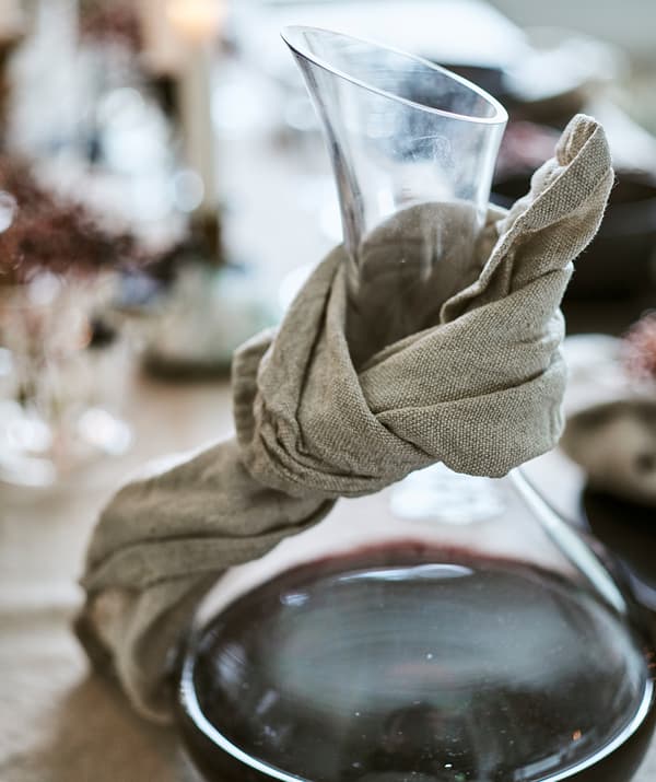 A glass carafe containing red wine with a natural coloured linen napkin tied round the neck to catch drips.