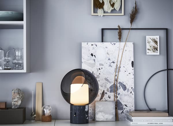 A glass table lamp, ornaments and artwork on a surface.