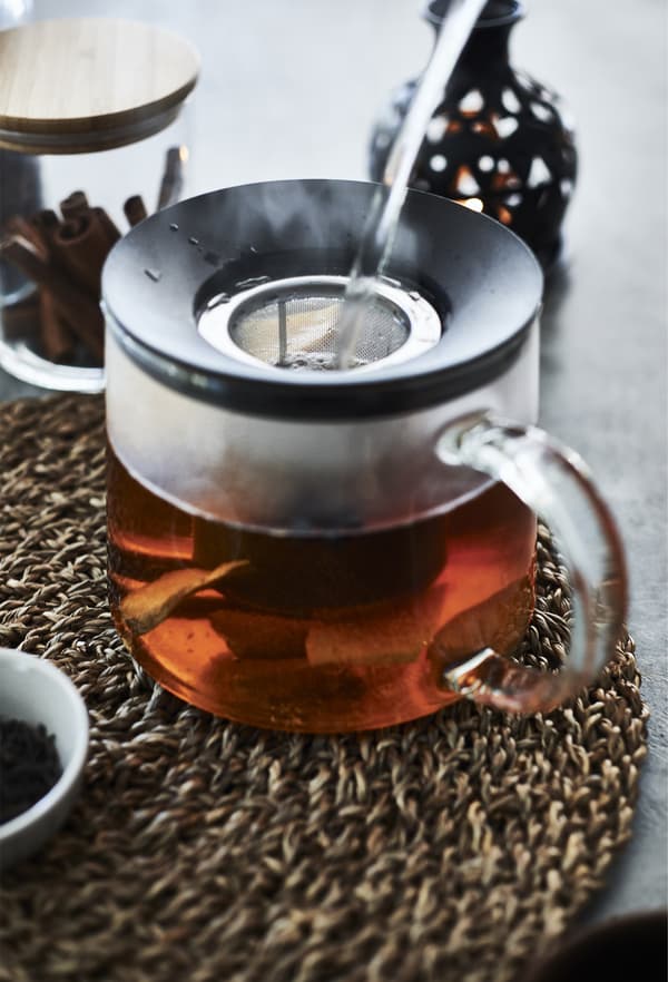 A glass teapot full of tea on a wicker mat.