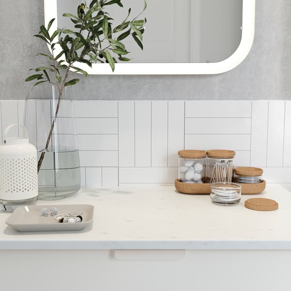 A glass vase, a bowl with jewellery and cotton swabs in a glass jar with cork lid stand on a countertop with marble effect.