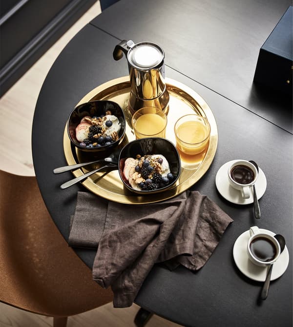 A GLATTIS round tray in brass-coloured, metallised stainless steel holds breakfast on a table in the bedroom.
