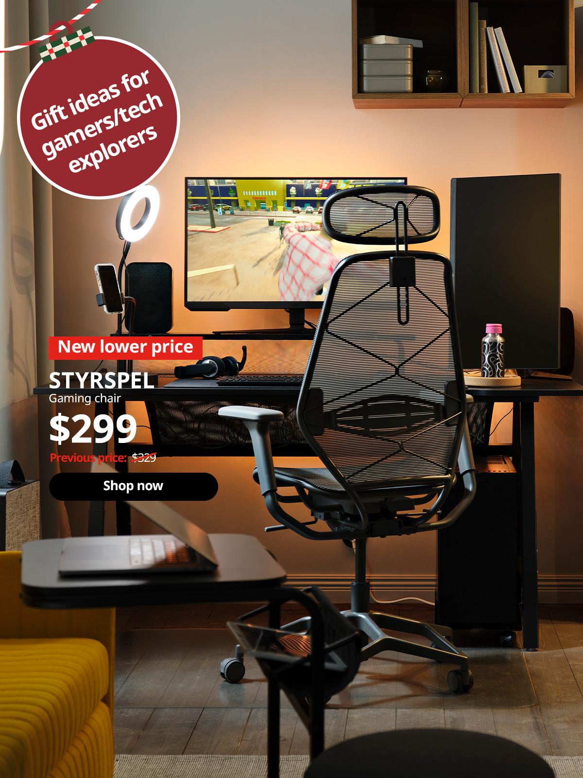 A glowing, backlit PC gaming setup has a paused game on a monitor on a black UTESPELARE gaming desk by a grey mesh chair.