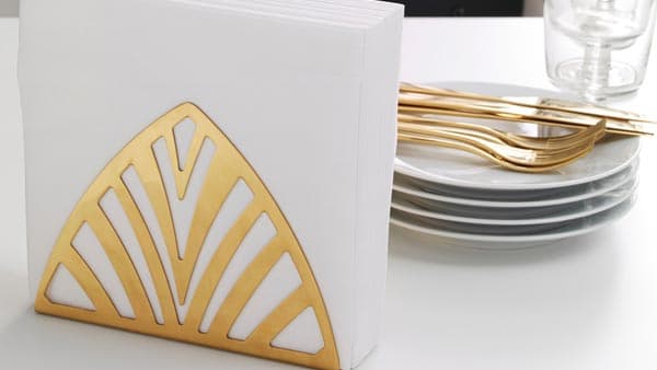 A gold napkin holder holding white napkins
