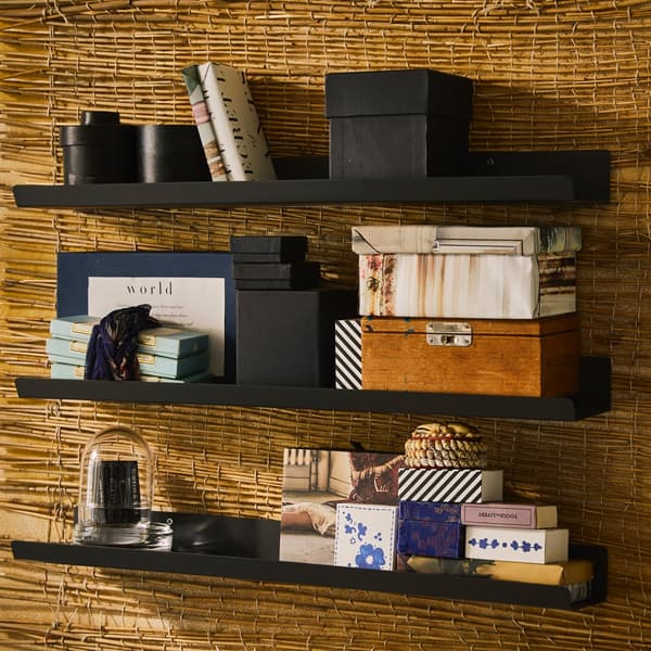 A gold wall with black wall shelves displaying decorated boxes, books and other decorations.