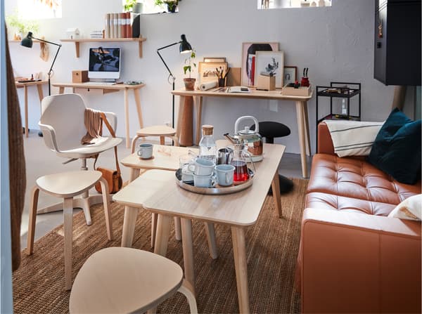 A golden-brown leather sofa, LISABO coffee table in ash veneer with a tray with mugs and three three-legged stools in birch.