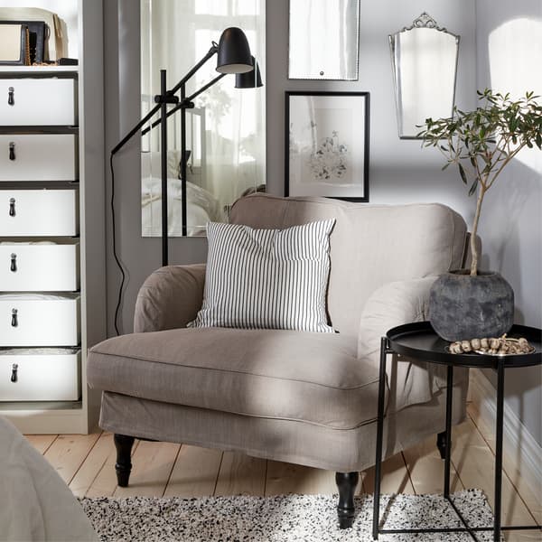 A gray-beige armchair, a black floor lamp, a striped cushion cover, a black tray table and a white rug.