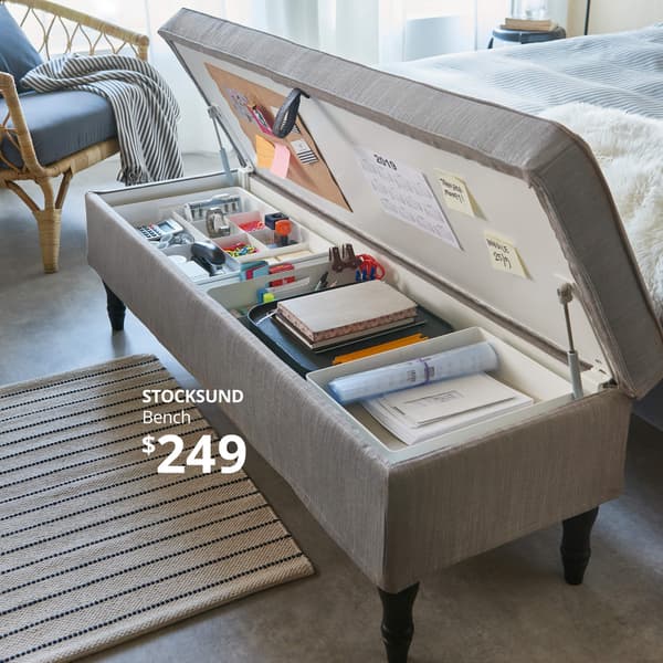 A gray bench with storage at the foot of a bed, holding an organized collection of school supplies. STOCKSUND Bench- $249