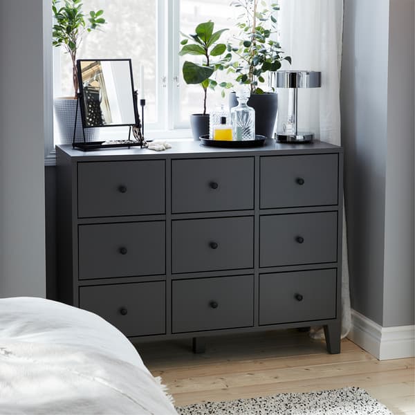 A gray chest of drawers, dark gray plant pots, green plants, chrome-plated table lamp and a black table mirror.